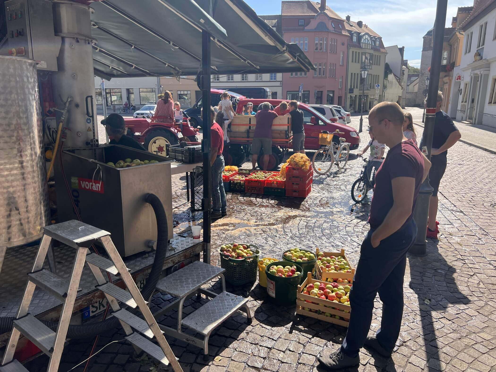 Ein junger Mann steht mit Äpfeln in Kisten vor dem Gerät, das den Most herstellt.