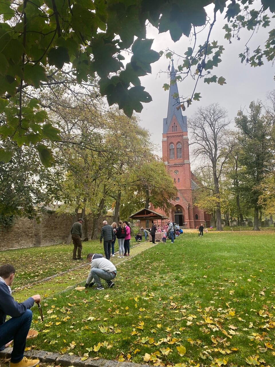 Blick auf einen Weg, der auf eine Kirche zu läuft. Menschen stehen auf und an dem Weg auf der Wiese.