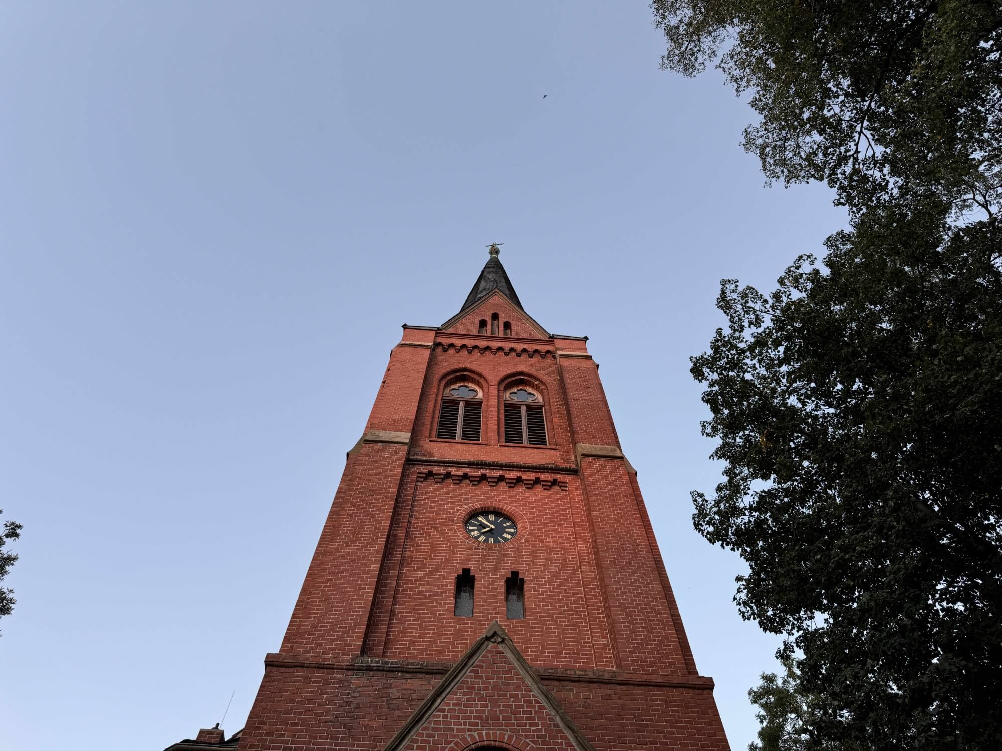 Ein roter Klinkerstein-Kirchturm vor blauem Himmel