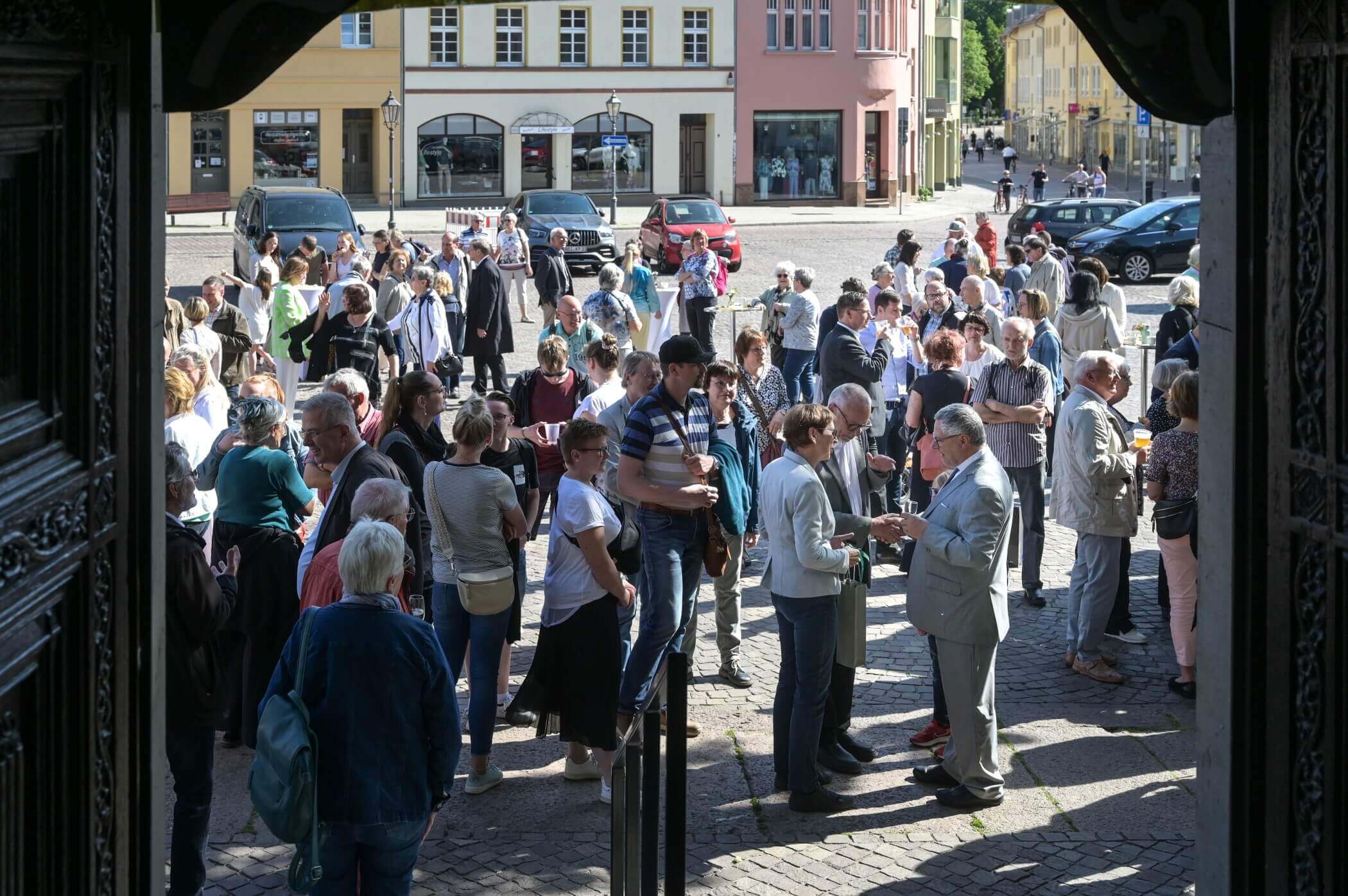 Blick durch die geöffnete Kirchentür auf einen mit vielen Menschen belegten Marktplatz.