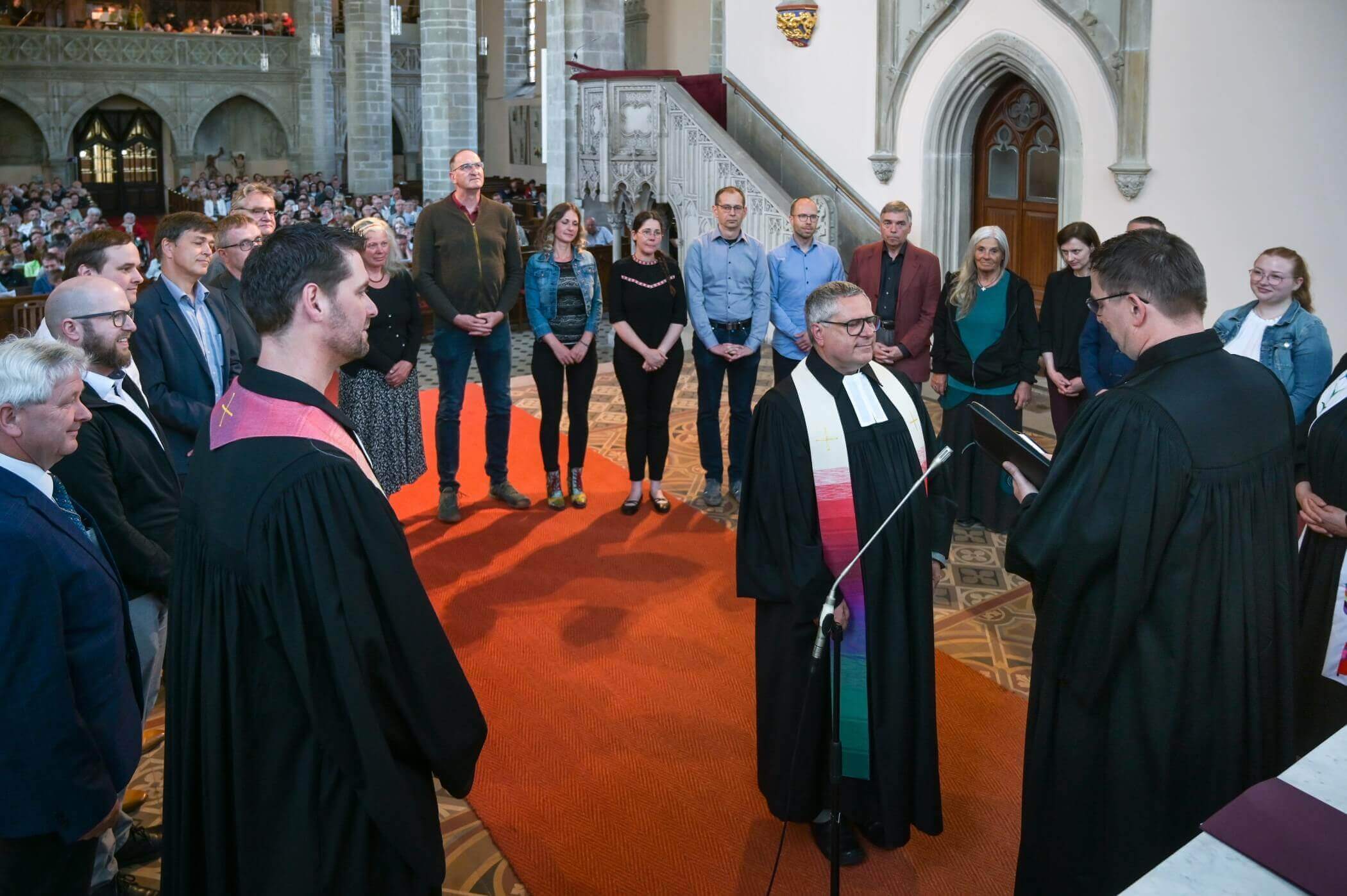 Menschen stehen im Altarraum im Kreis um einen Pfarrer herum im Hintergrund ist die vollbesetzte Kirche zu sehen