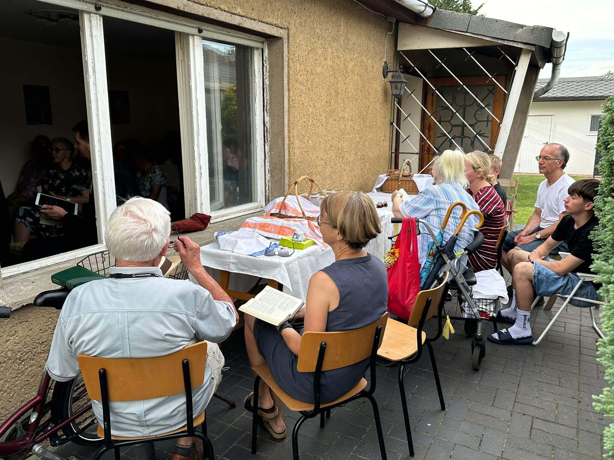 Menschen sitzen außen vor einem geöffneten Fenster