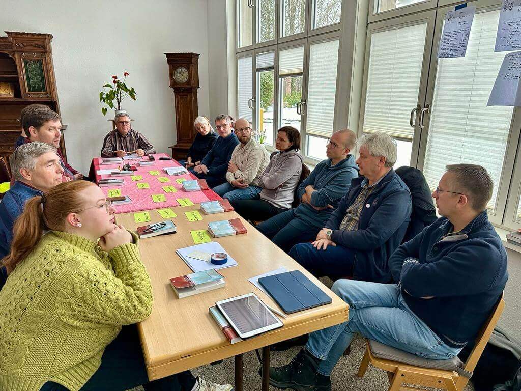 Menschen sitzen um einen Tisch auf dem Zettel mit Aufgaben liegen