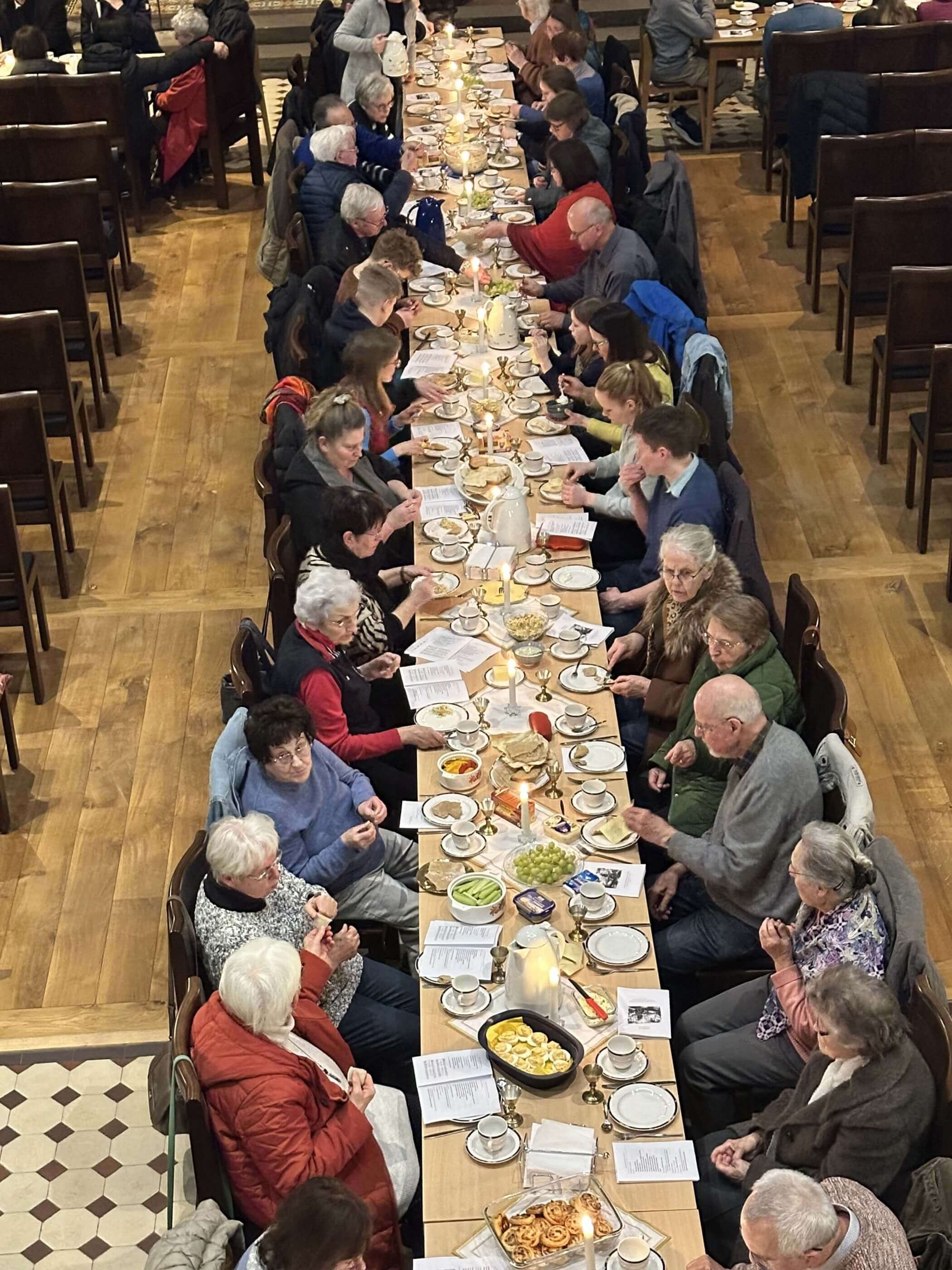 Ein Blick von oben auf eine lange Tafel an der viele Menschen sitzen, essen und sich unterhalten