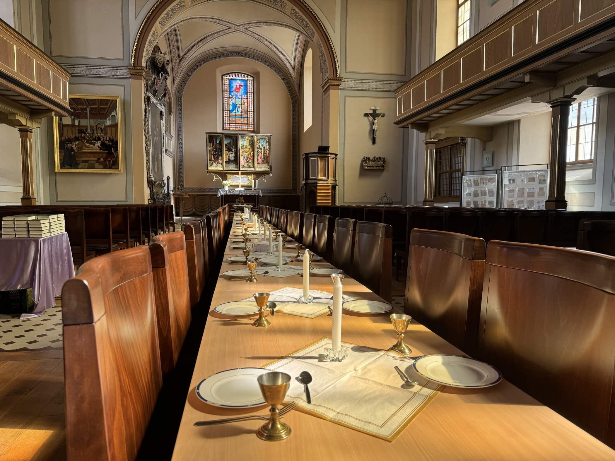 ein gedeckter Tisch mit Kerzen, Tellern und Kelchen in einer Kirche mit Blick auf den Altar