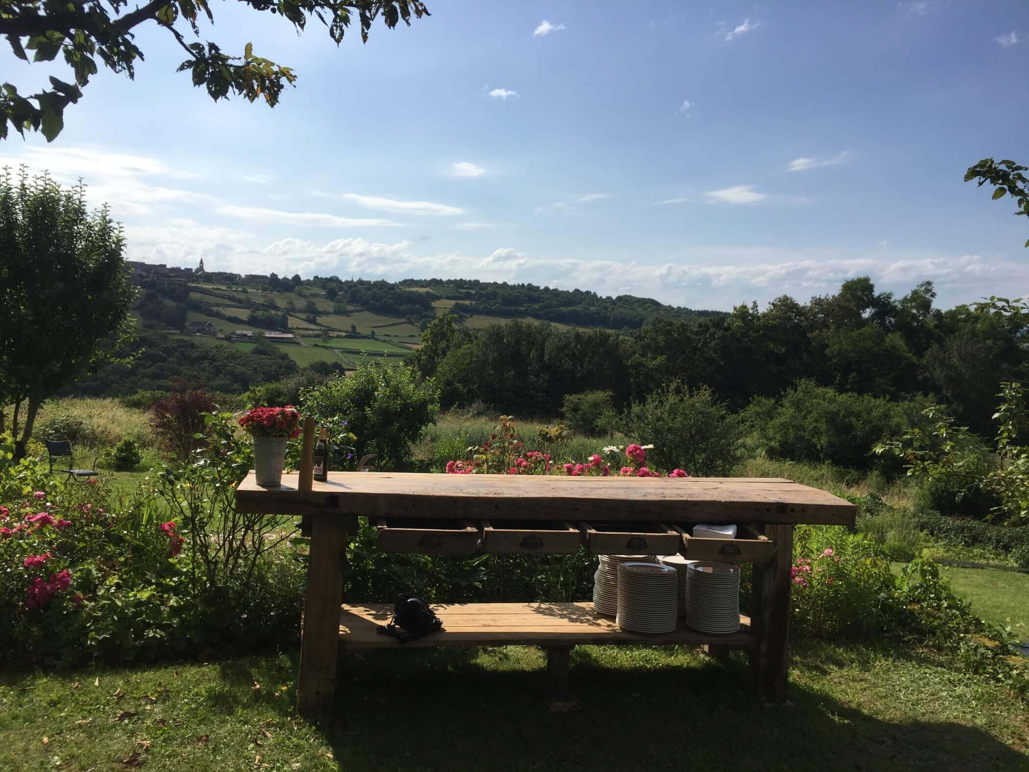 Ein schwerer Holztisch auf einer Wiese, dahinter Blick in die Landschaft des Burgund