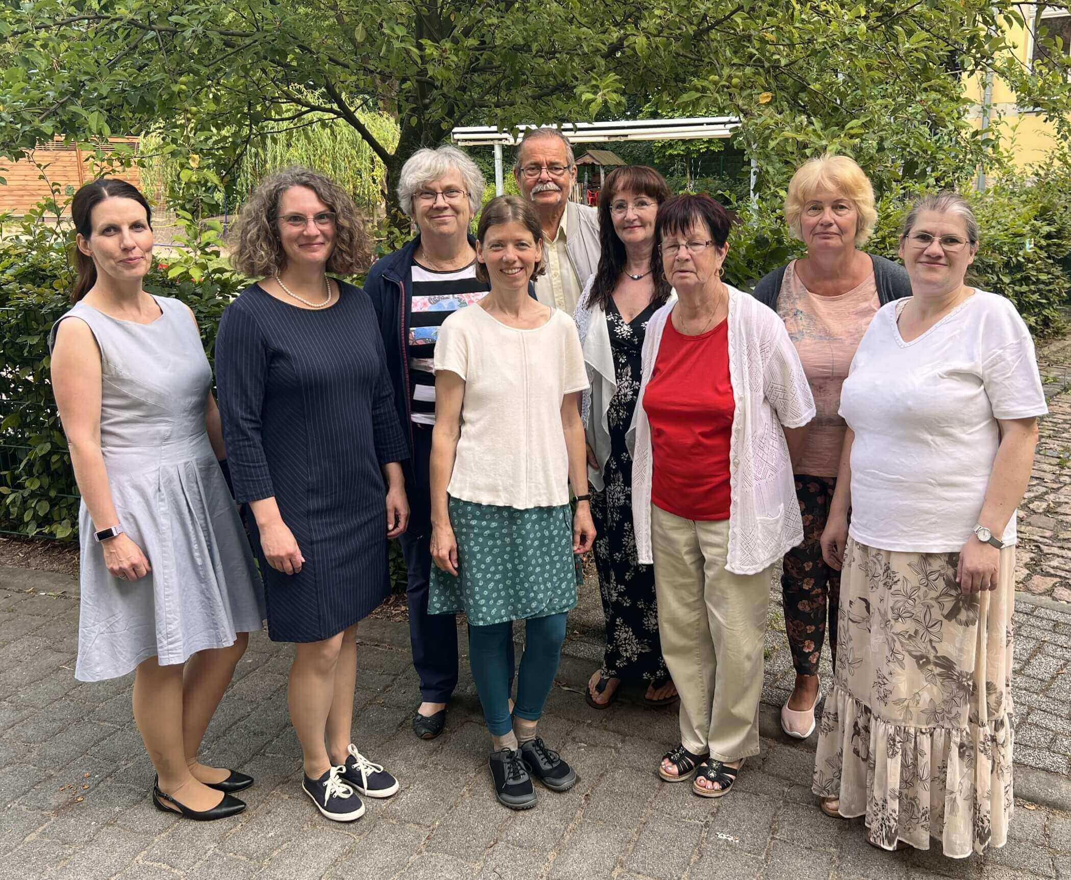 9 Menschen vor einem Baum auf grauem Pflaster stehend